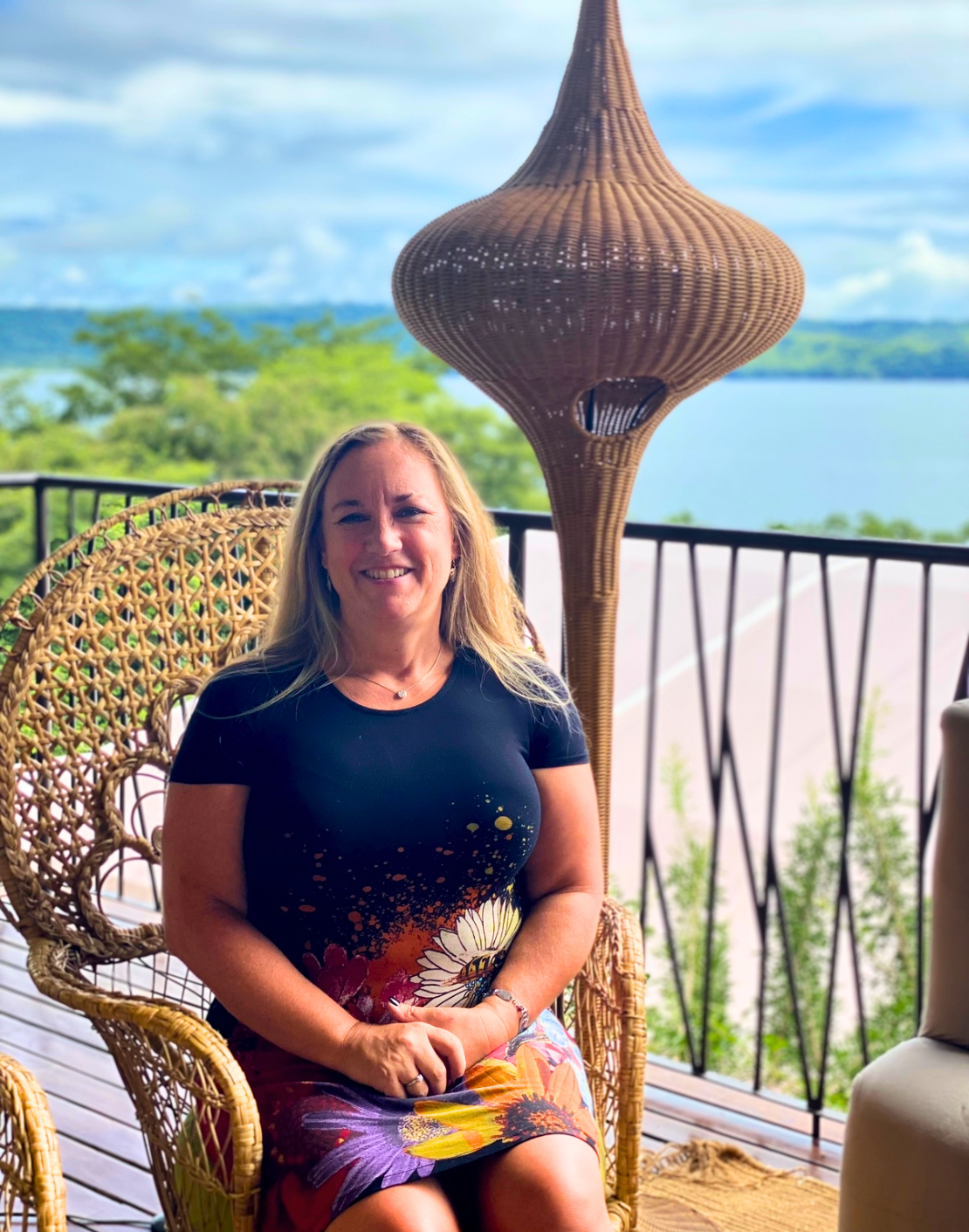 An image of Ronda, a travel agent, sitting on a chair on a balcony overlooking the water. 